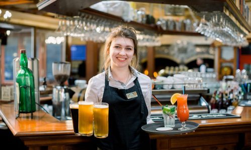 Smiling friendly waitress serving a pint of draft beer in a pub. Portrait of happy young woman serving beer in bar, looking at camera smiling.